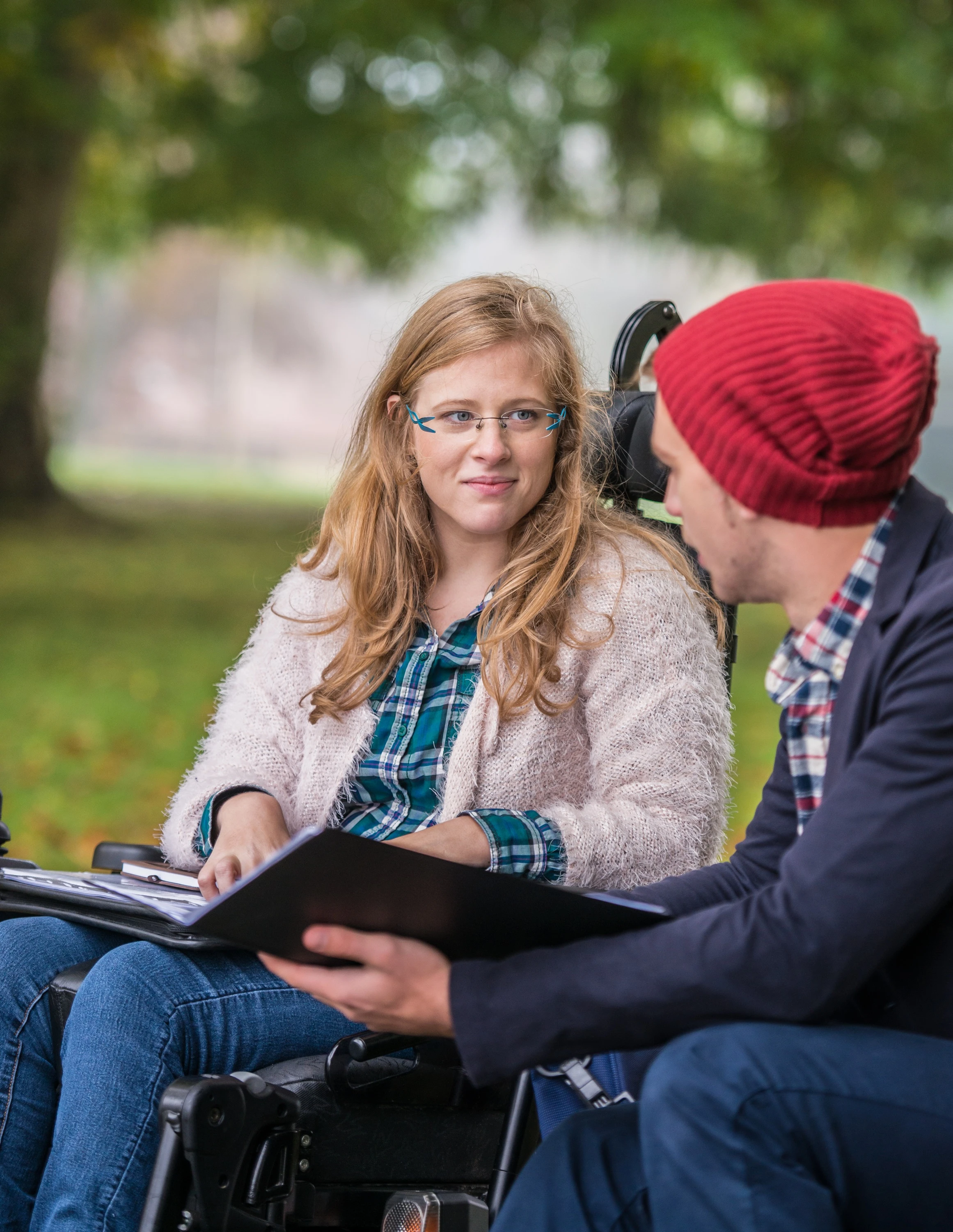 Junge Frau im Rollstuhl sitzt mit Assistent im Park